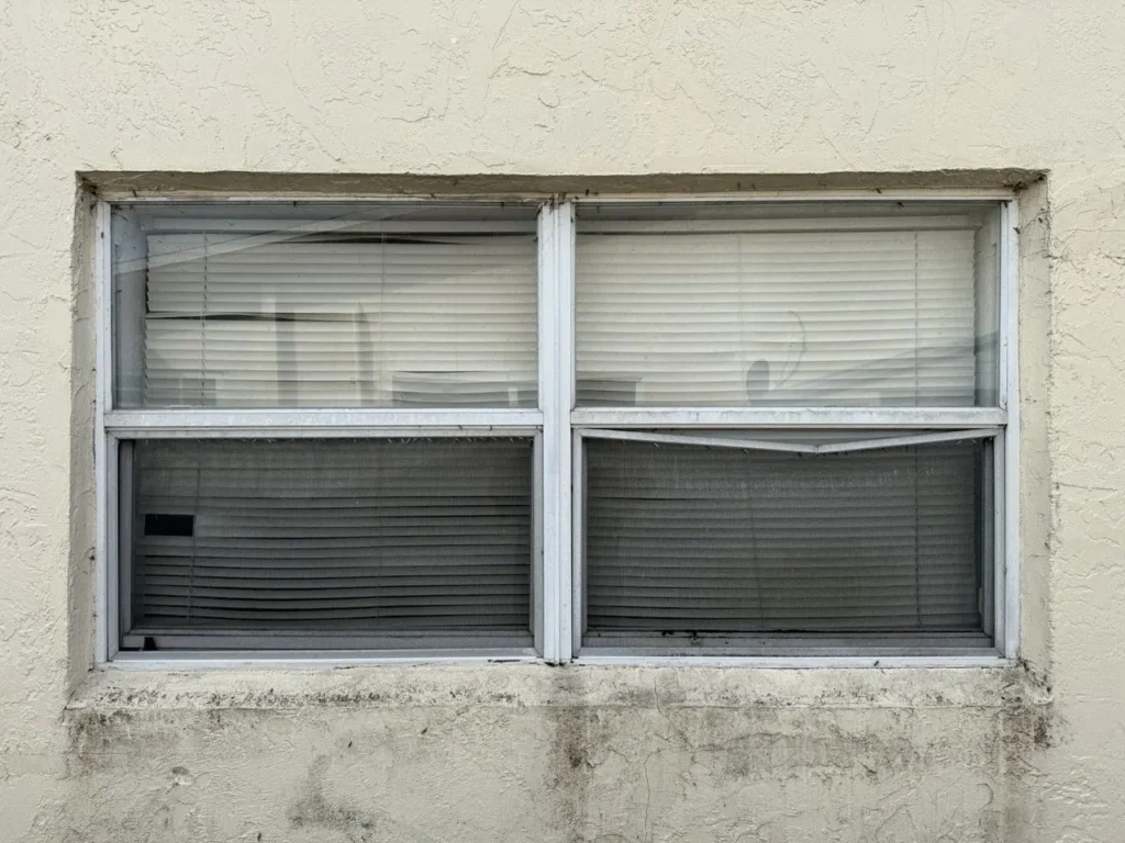 Old aluminum window with blinds in Broward County before replacement