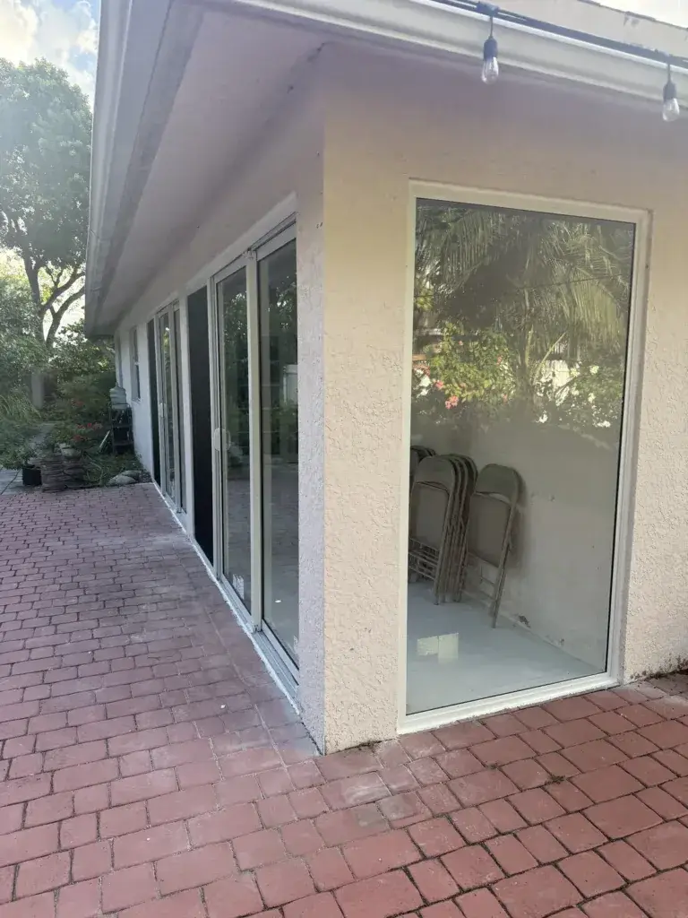 Patio fully enclosed with floor-to-ceiling impact glass windows, exterior view along the paver deck