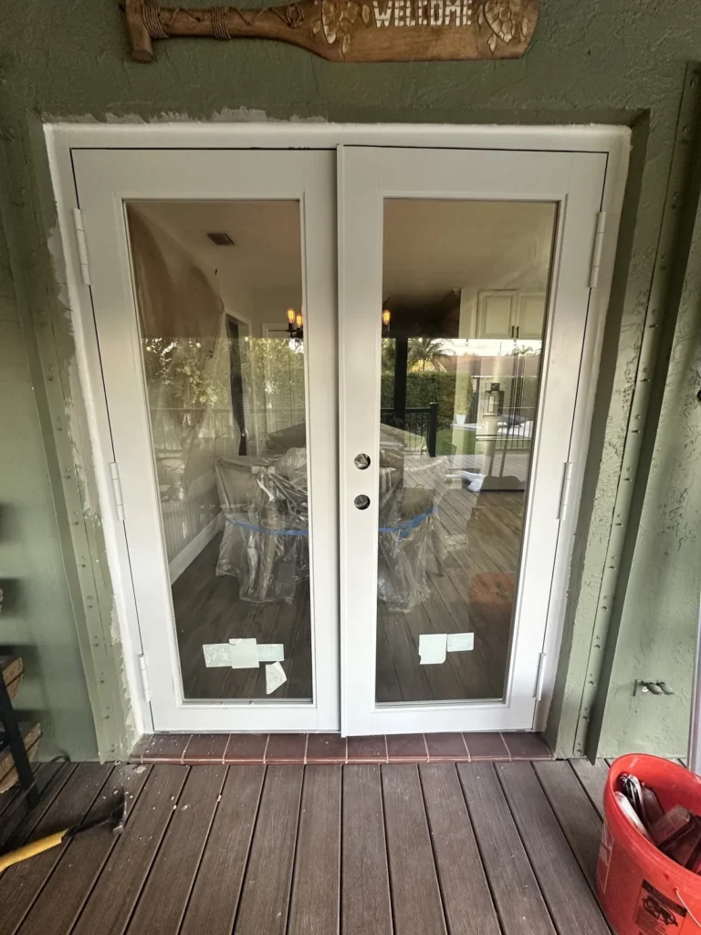 Newly installed impact French doors to a deck, manufacturer labels still on the glass